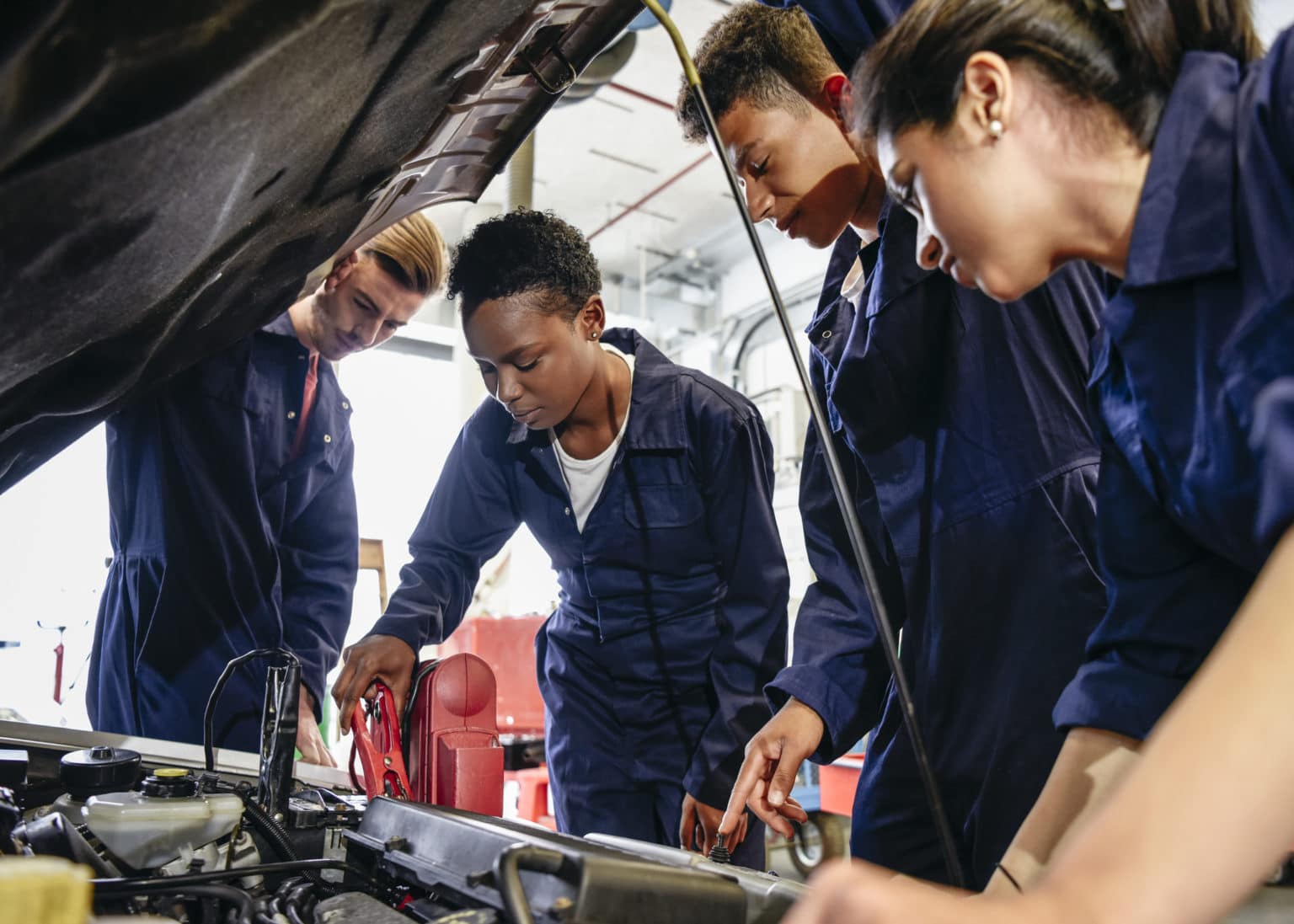a group of multi ethnic mechanical apprentices working on a car