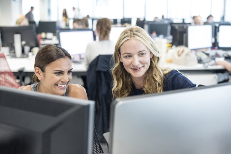 Two women working in office looking at computer, smiling